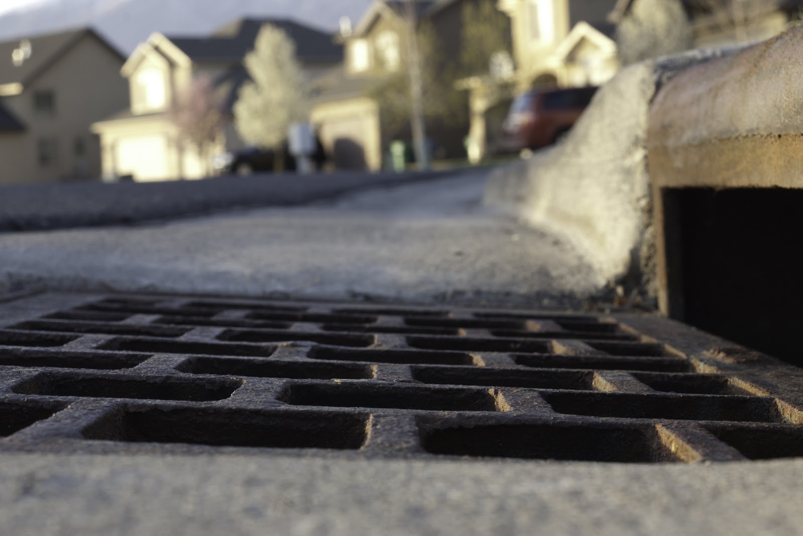 a storm drain with a drainage grate on a curb in a suburban neighborhood